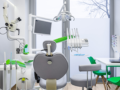 The image shows a modern dental office interior with various pieces of equipment and furniture, including chairs, a desk, a computer monitor, and a dental chair.