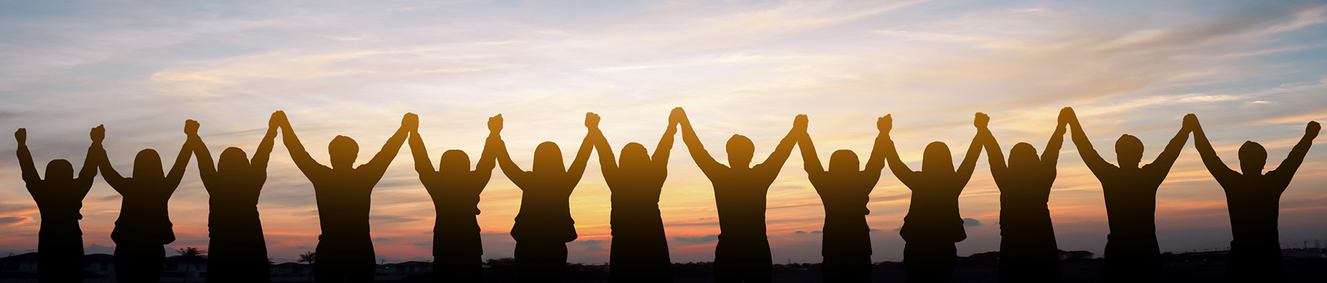 The image shows a group of people standing together with their hands raised, creating an arc, against a sunset sky.