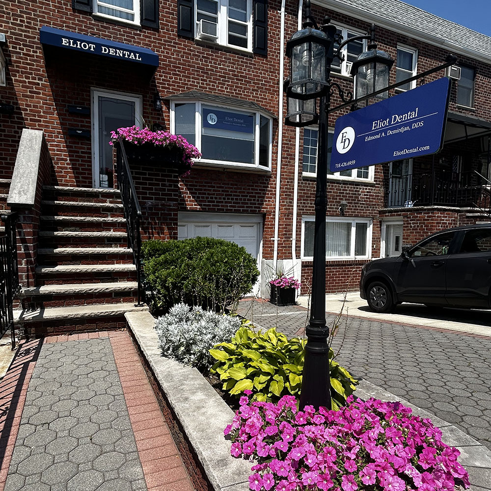 The image shows a street scene with a sign for a dental practice, a building with a blue and white sign, a tree, flowers, and a sidewalk with steps leading up to it.