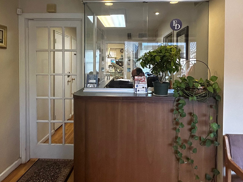 The image shows an interior view of a room with a reception desk, a potted plant, and a glass door.