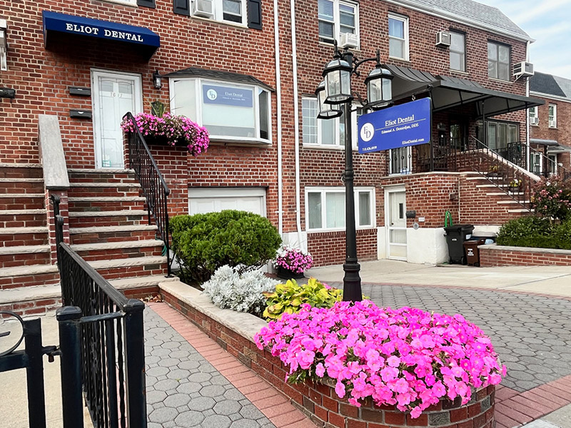 The image shows a street corner with a building labeled  Eliot Dental  and a sign for an apartment complex, featuring a parking lot, stairs, and flowers.