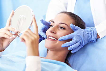 Woman undergoing cosmetic dermatology treatment with medical professional holding mirror over her head for examination.