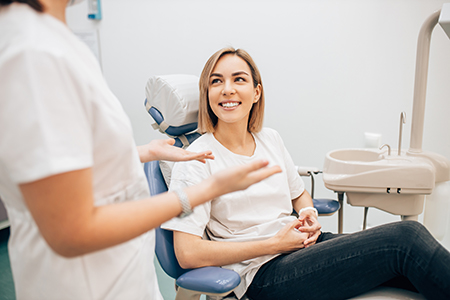 A woman sitting in a dental chair with a smile on her face, being attended by two dental professionals who are engaged in conversation.