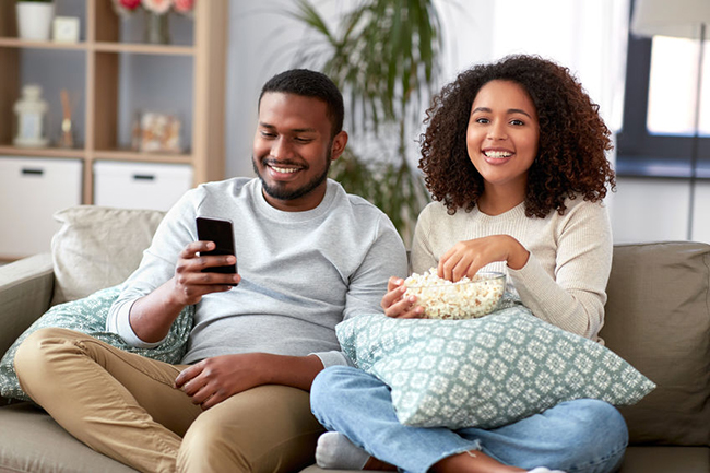A man and woman sitting on a couch, enjoying a movie together with popcorn.